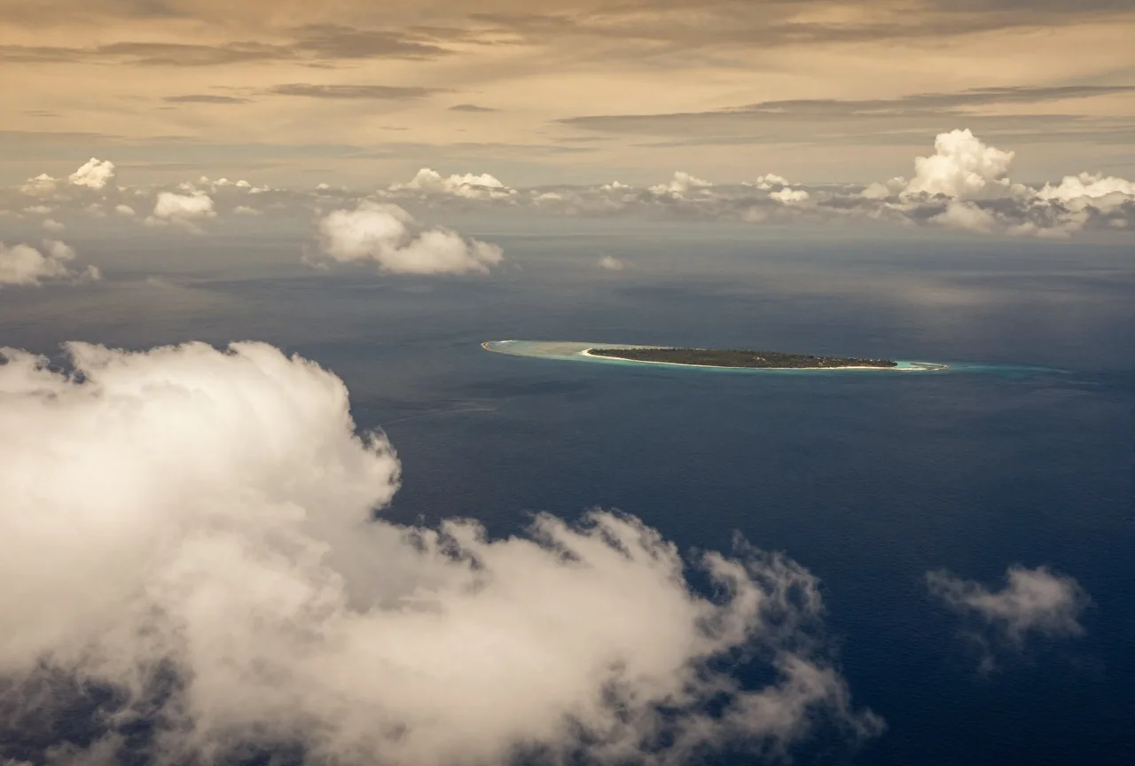 Der offene Pazifik von oben mit hohen Quellwolken und einer kleinen flachen Koralleninsel am Horizont