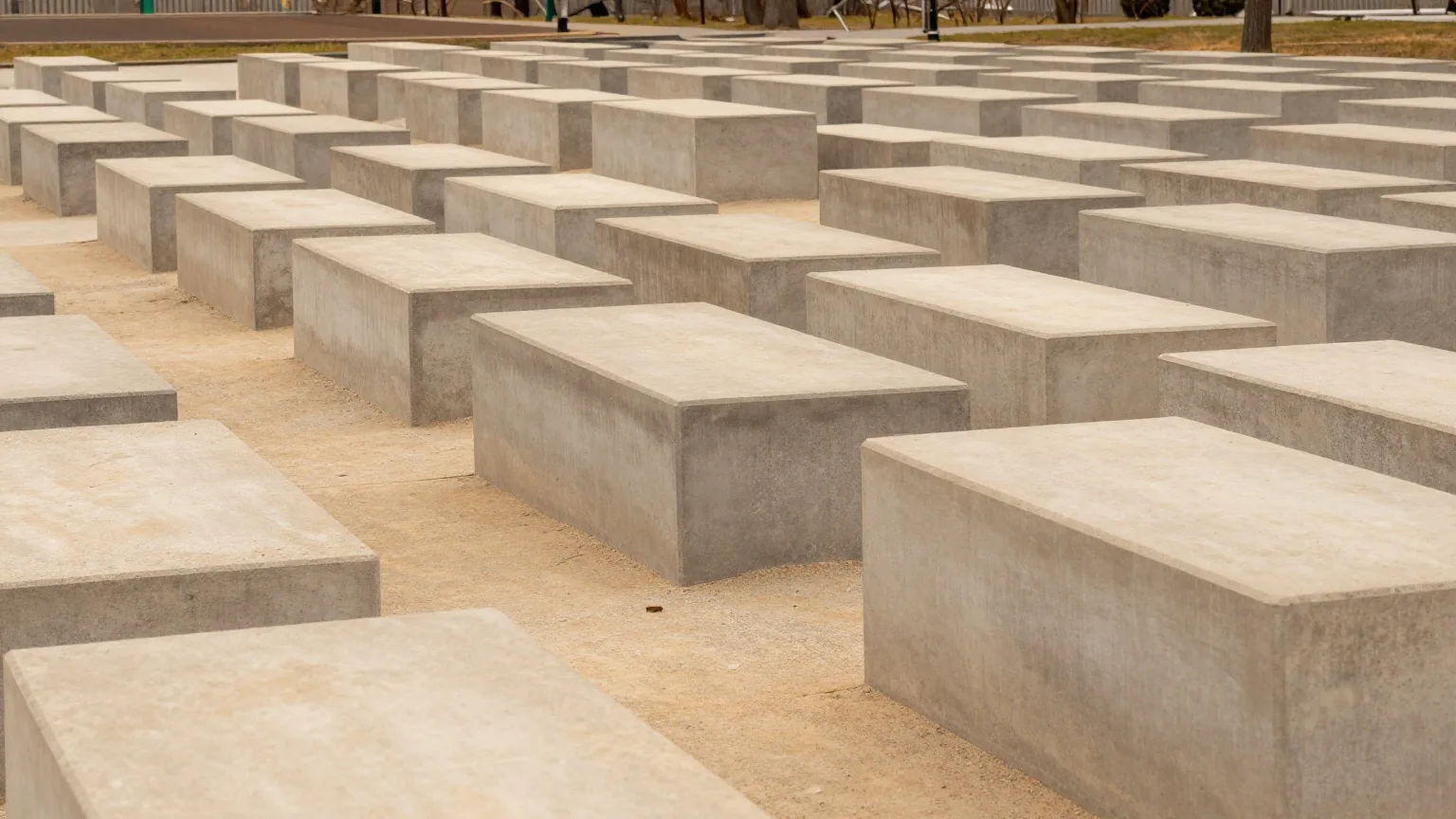Ein Feld aus schlichten grauen Betonquadern unterschiedlicher Höhe im trüben Licht, schmale Wege dazwischen