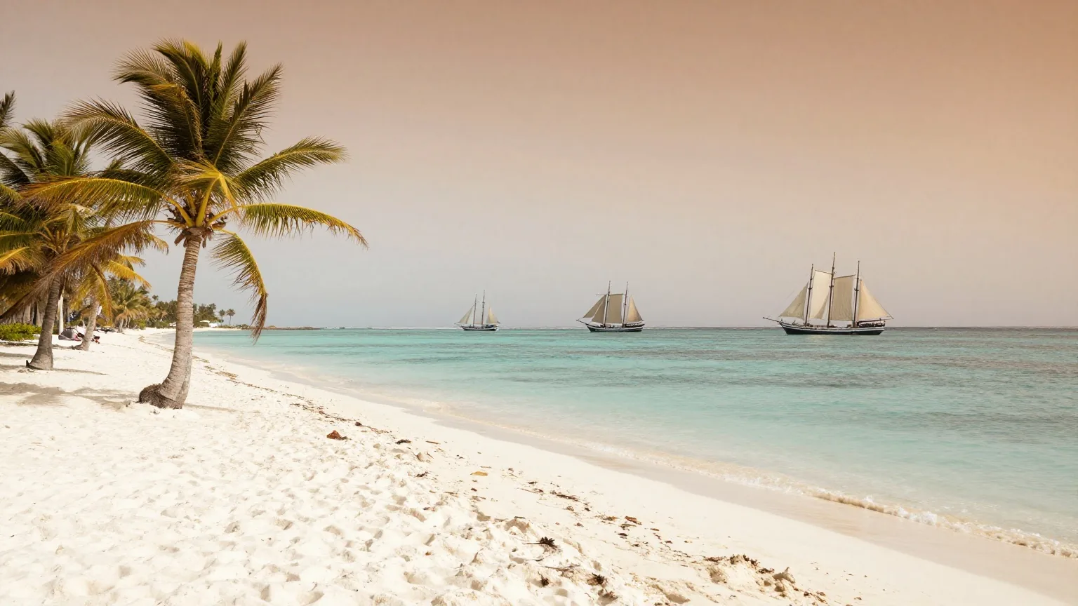 Ein weißer Sandstrand einer Karibikinsel bei Sonnenaufgang mit Palmen und drei Segelschiffen weit draußen