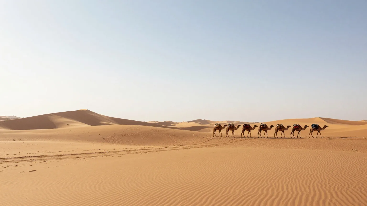 Eine Karawanenroute durch goldene Sanddünen bei Sonnenaufgang mit einer Reihe Kamele in der Ferne