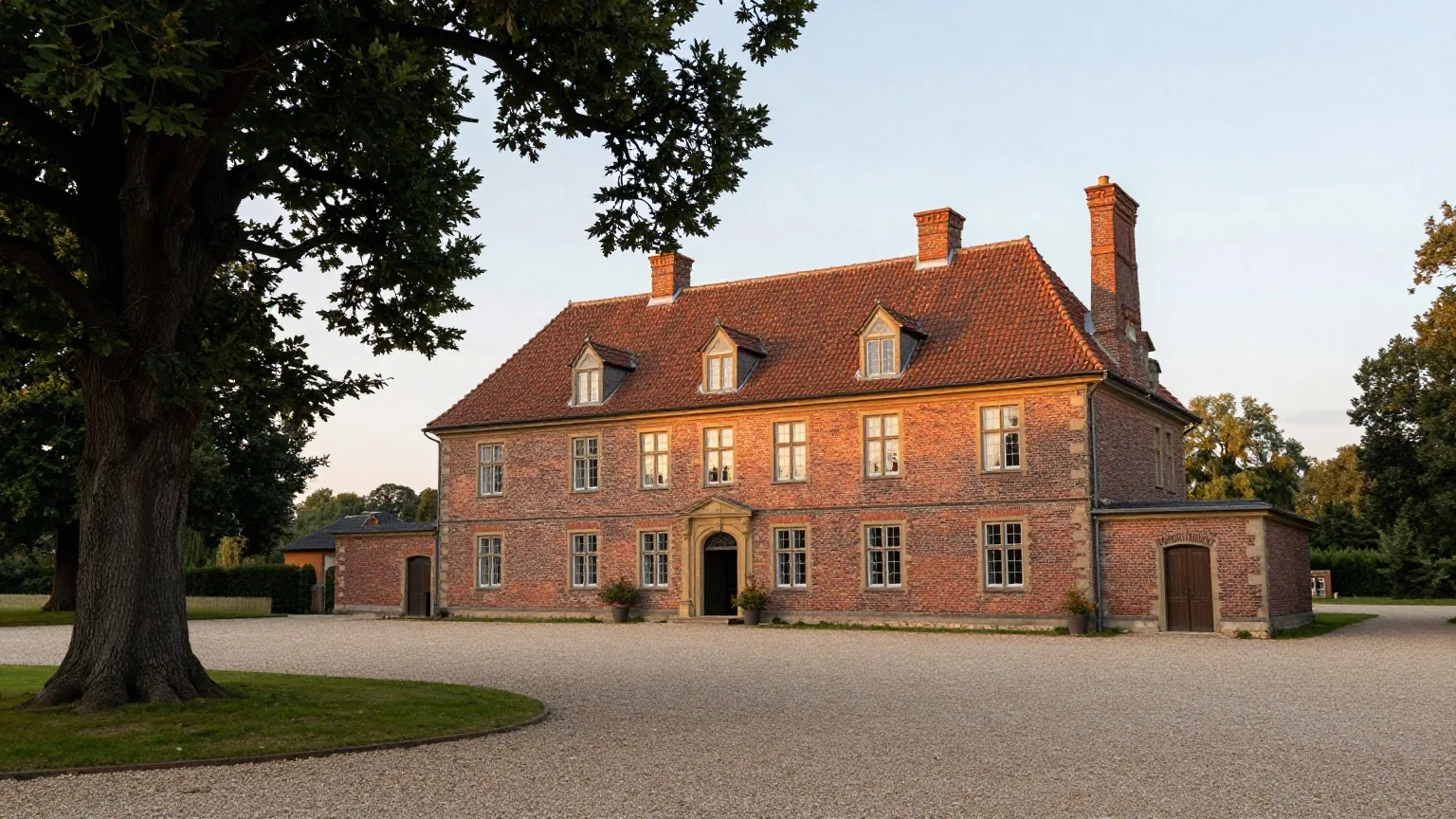 Ein ruhiges Gutshaus in der flachen Altmark im Spätsommer mit Backsteinmauern, alten Eichen und Kiesweg