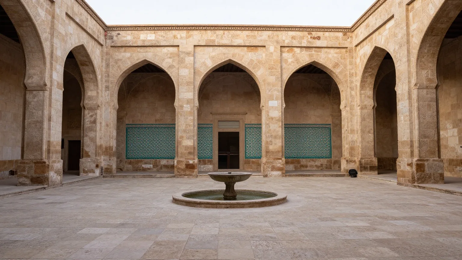 Ein stiller Innenhof mit Spitzbögen, türkis und weiß gemusterten Fliesen und einem runden Brunnen in der Morgendämmerung